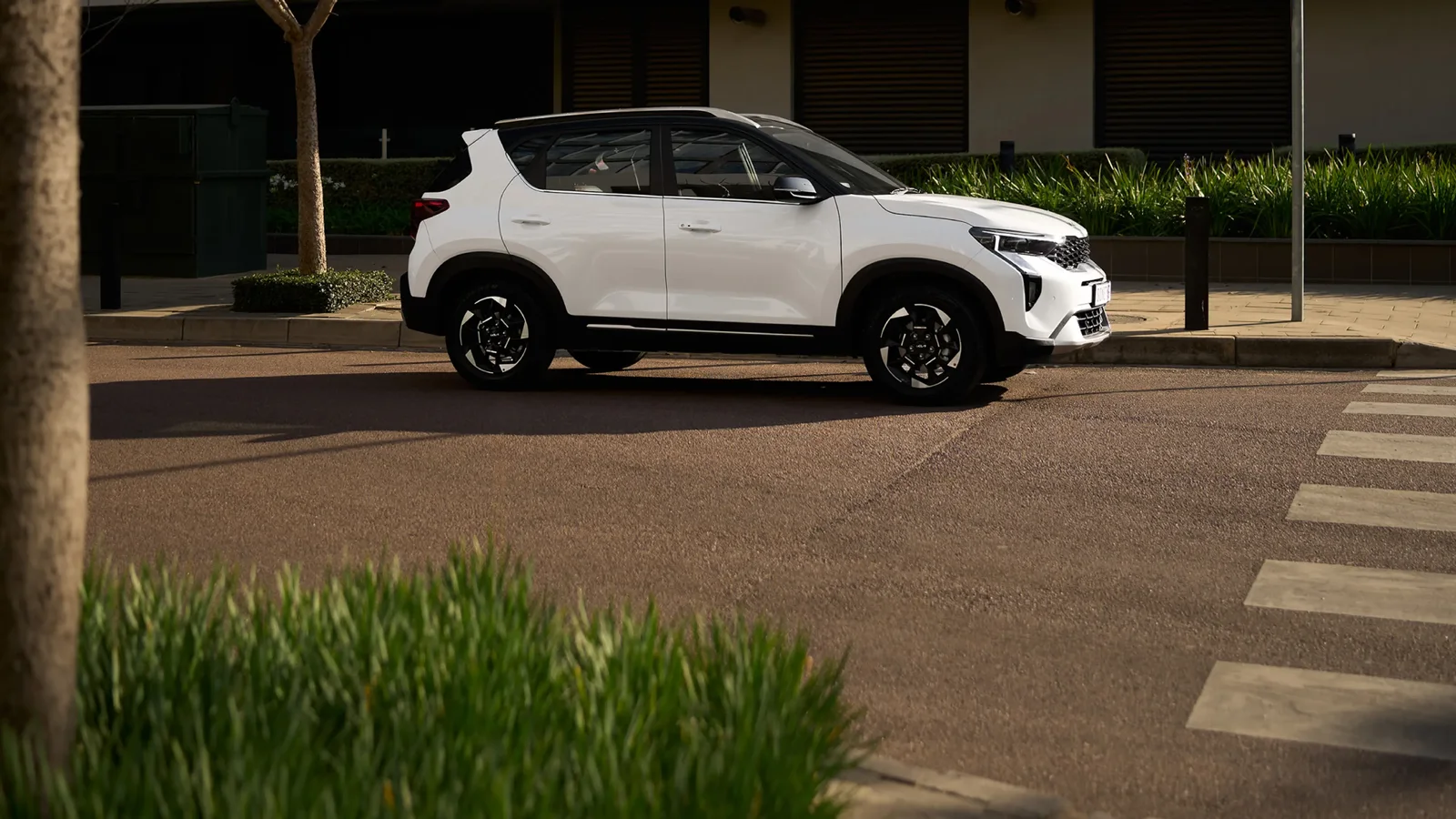 White Kia Sonet compact SUV on a leafy city street
